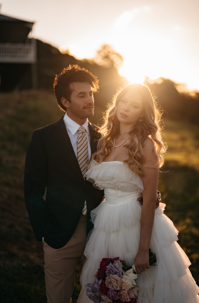 Man and woman in formal attire standing together with a sunset background