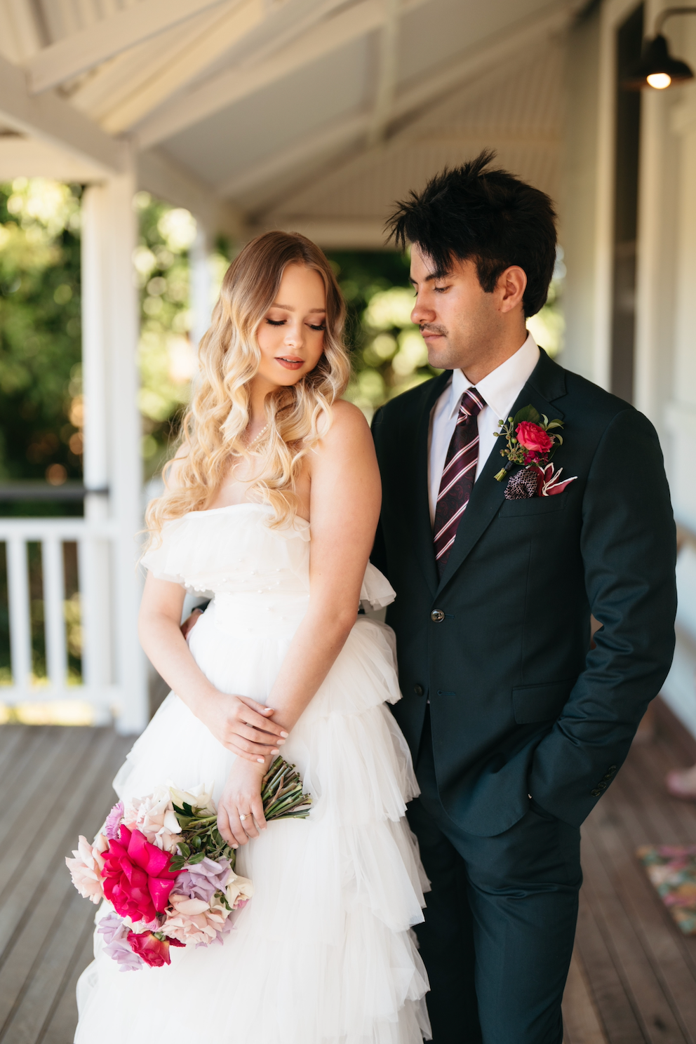Man in a suit and woman in a wedding dress standing on a porch.