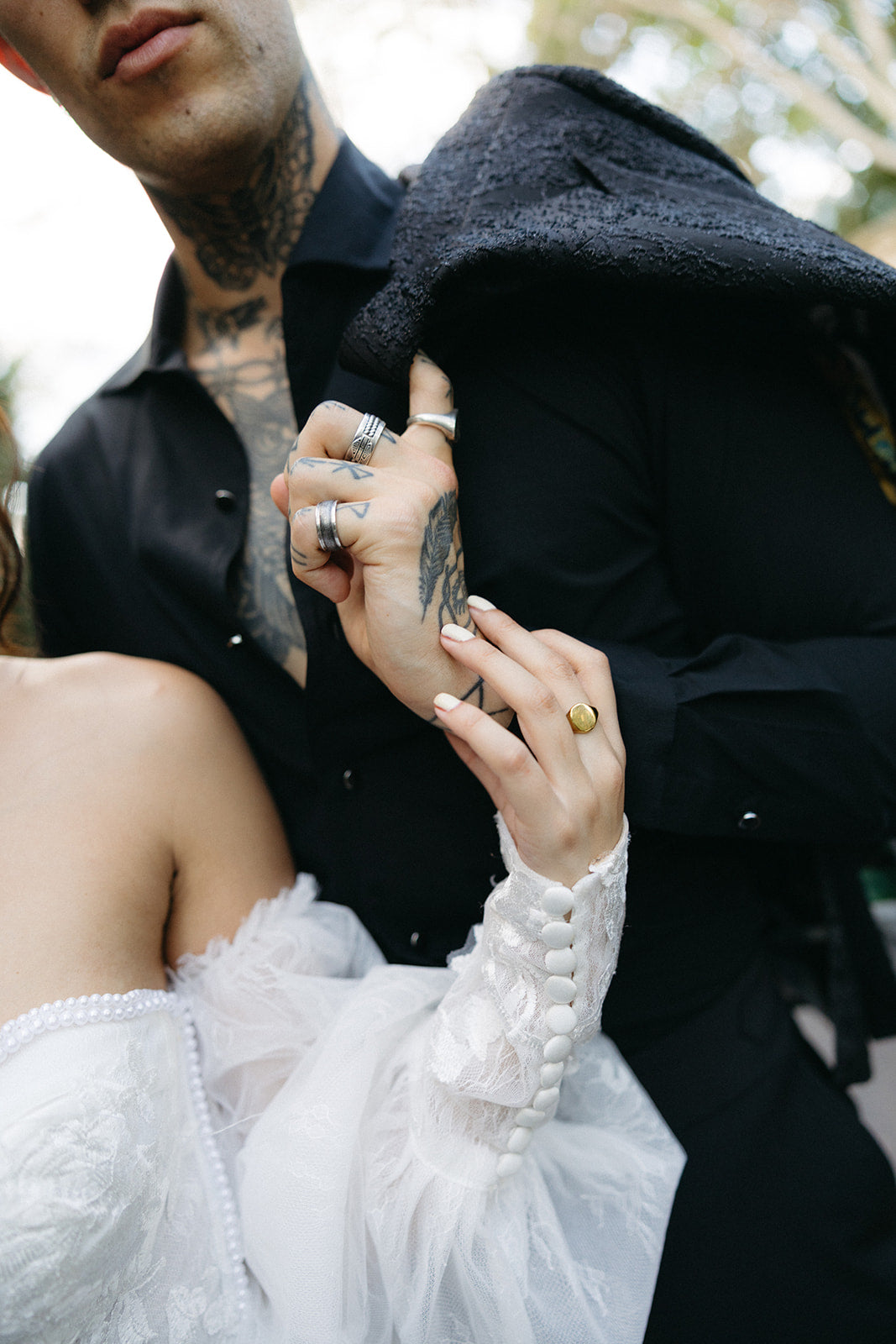 Person in a black outfit with tattoos holding hands with another person in a white outfit.