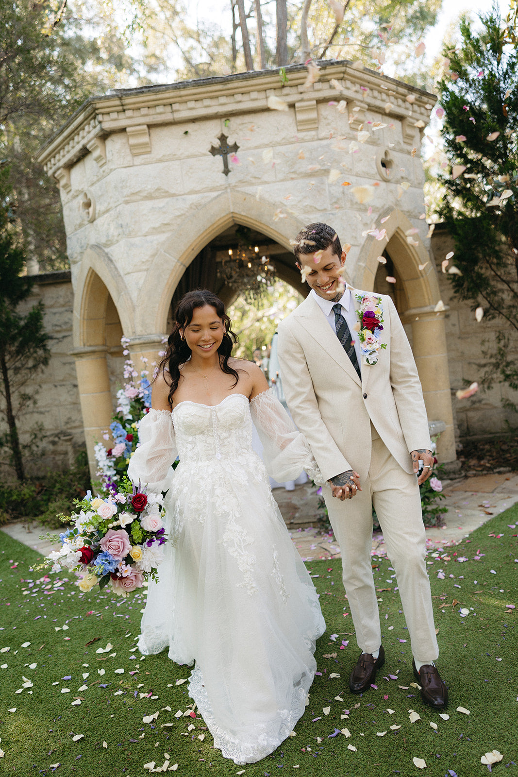 Wedding couple standing in front of a stone archway with floral decorations.