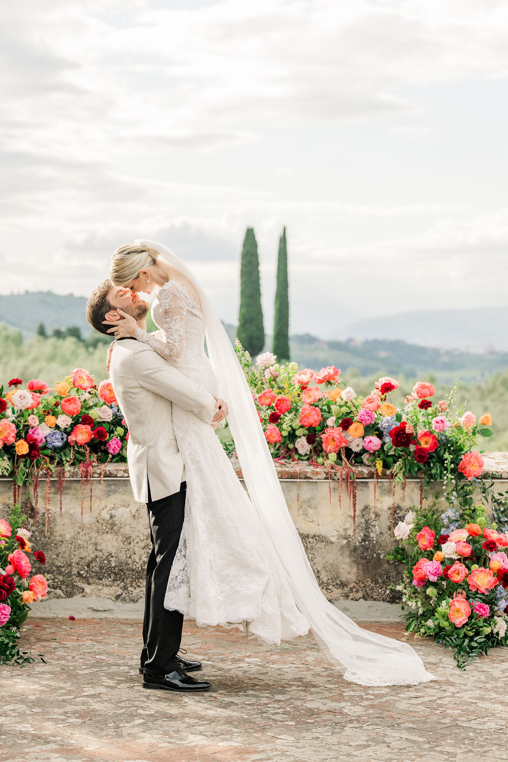 Couple embracing in a romantic setting with colorful flowers and a scenic background