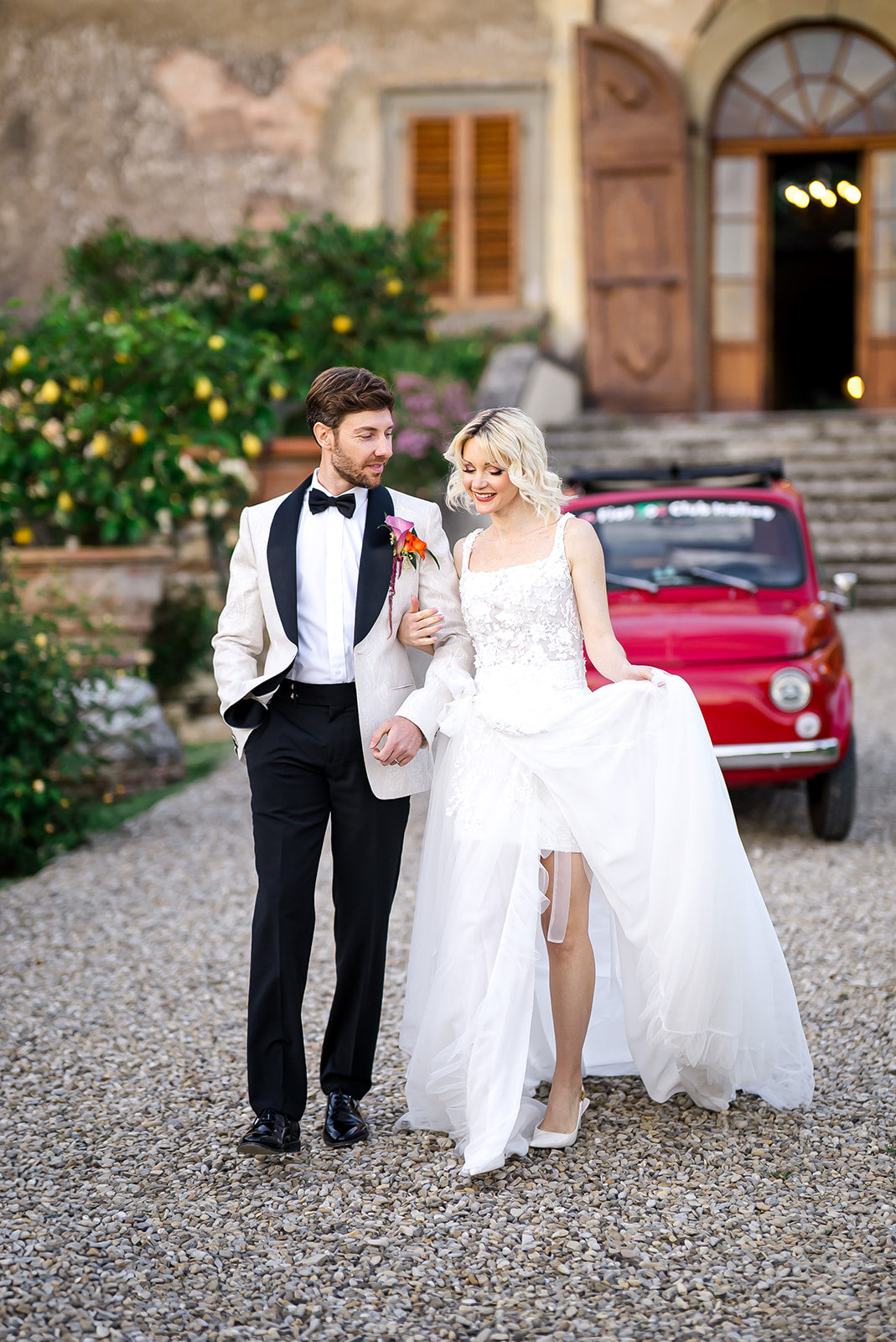 Wedding couple walking together in a picturesque setting with a red car in the background.